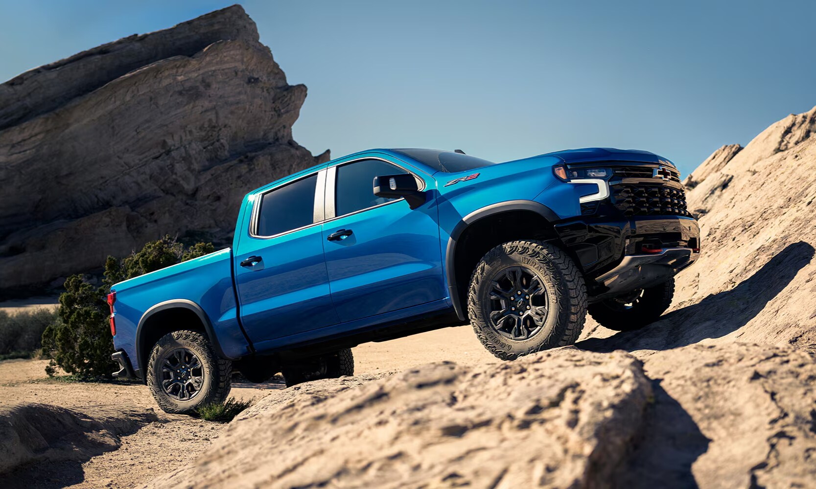 Exterior side image of a blue 2025 Chevy Silverado 1500 parked on a steep rocky hill in a natural landscape