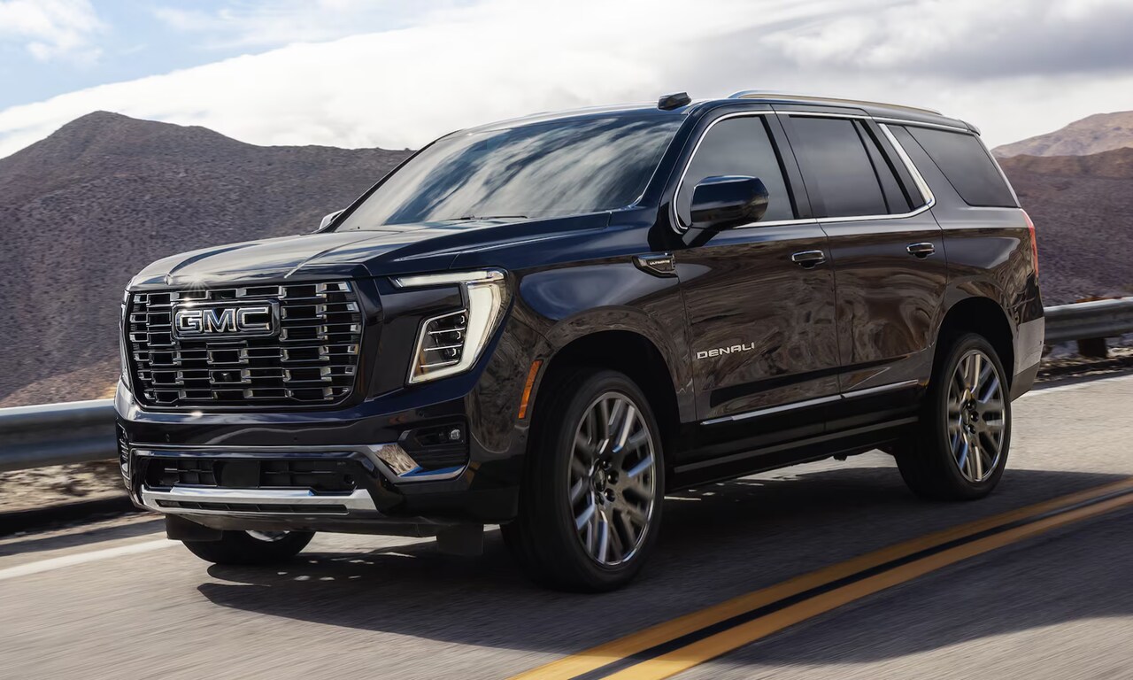Exterior image of a black 2026 GMC Yukon Denali driving on an open mountainous freeway