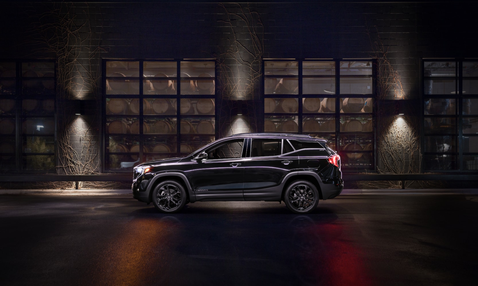 Exterior side image of a black 2021 GMC Terrain SLT Elevation Edition parked in front of an industrial building at night