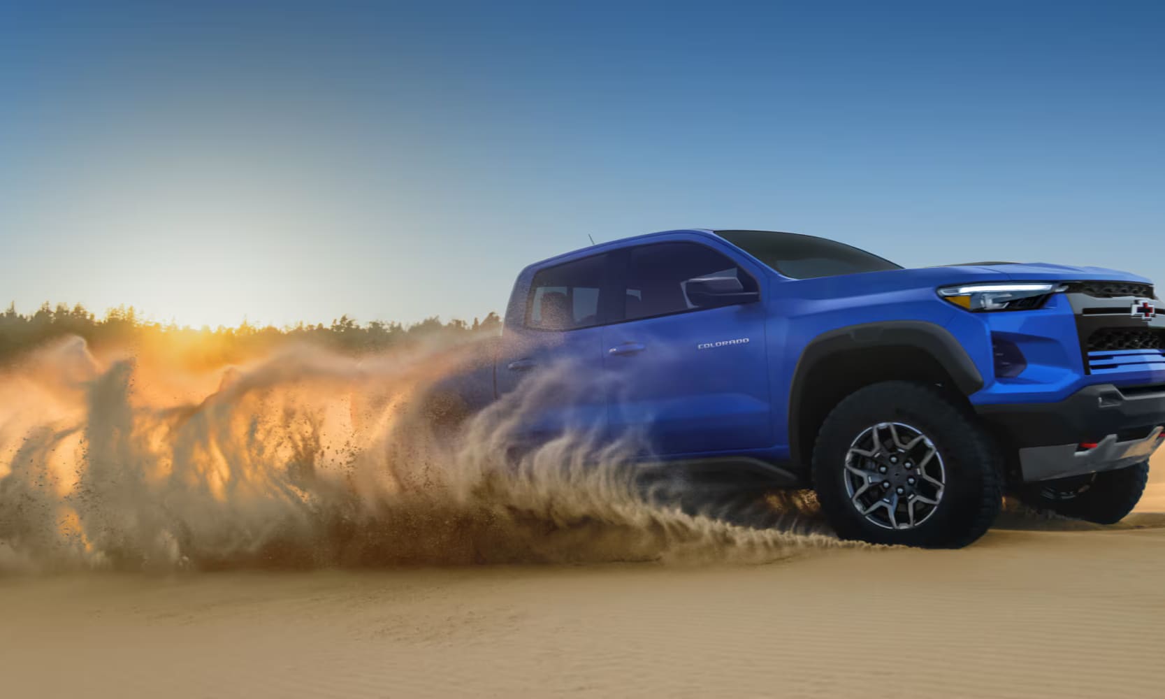 Exterior side image of a blue 2026 Chevy Colorado off-roading in a desert with sand blowing behind the wheels