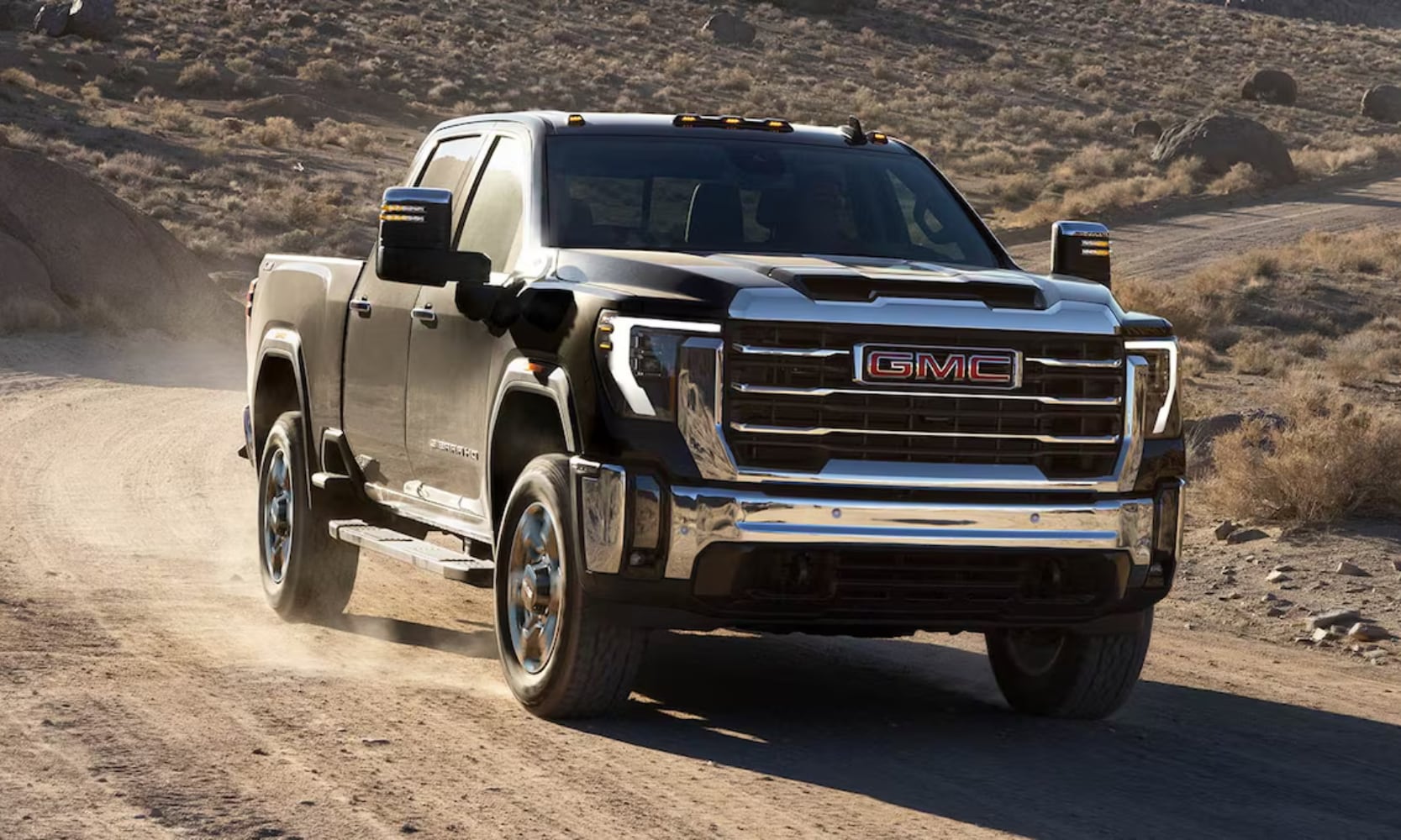 Exterior front view image of a black 2026 GMC Sierra 2500 HD SLT driving down a dirt road