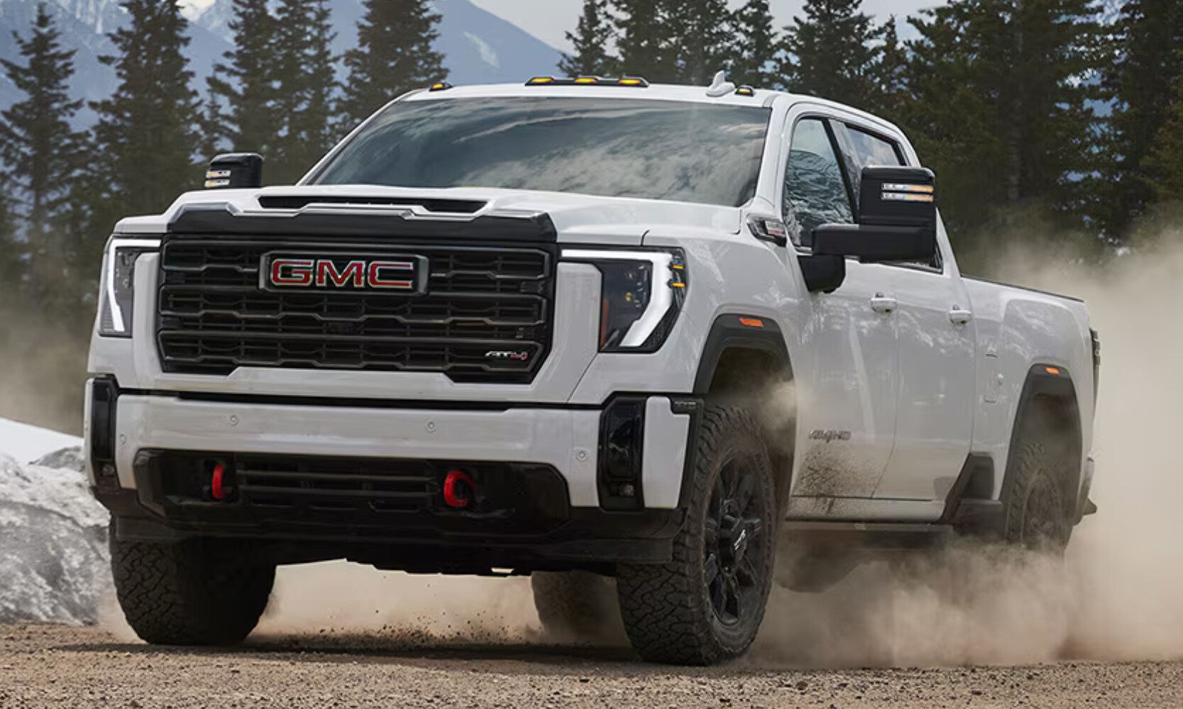 Closeup exterior image of a white 2026 GMC Sierra HD AT4 blowing dirt in a forest mountain landscape