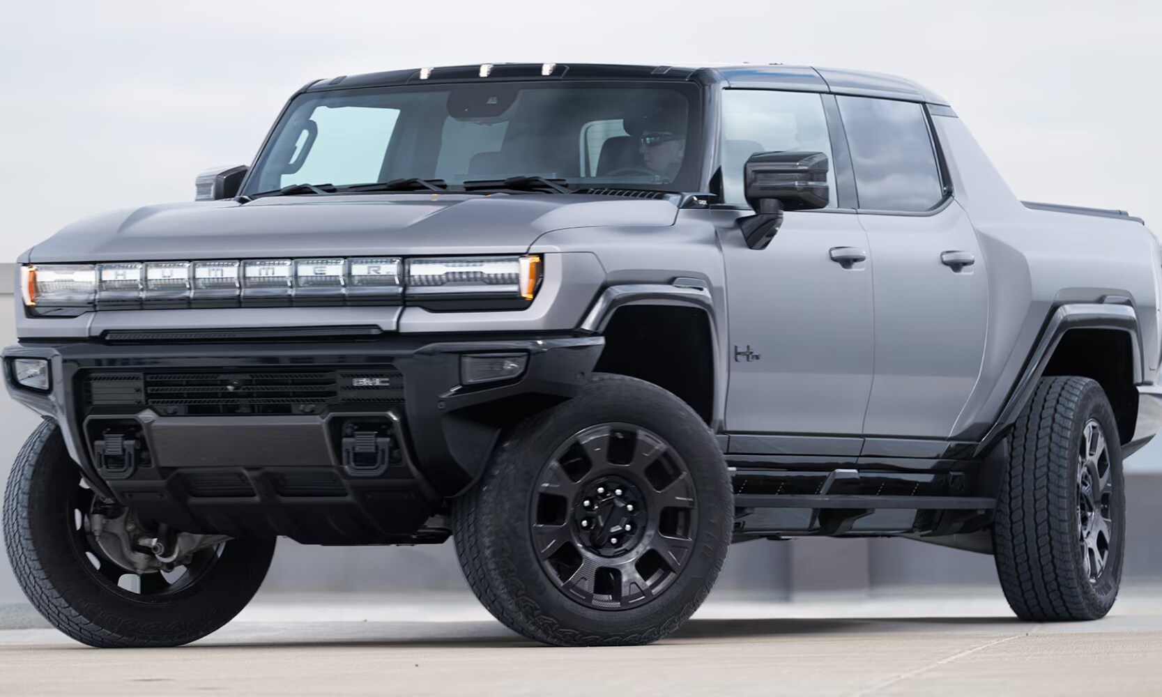 Exterior front angle image of a gray 2026 GMC Hummer EV Pickup parked on a parking garage rooftop