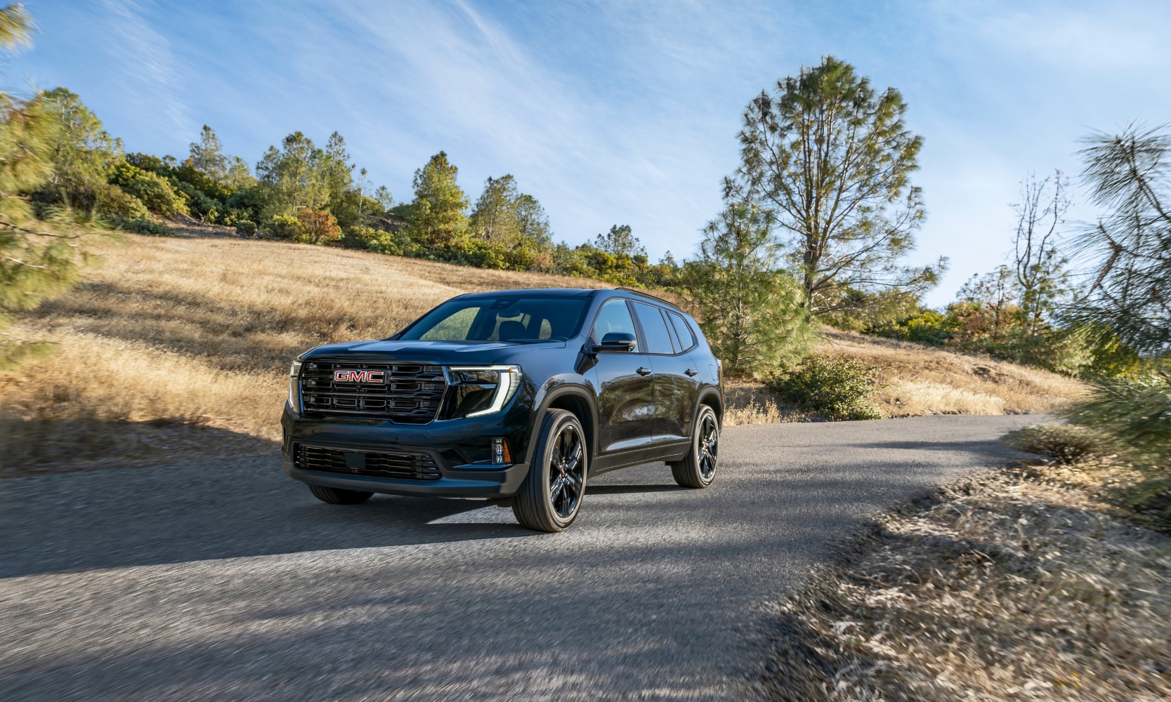 Exterior image of a black 2024 GMC Acadia Elevation Black Edition parked on a rural road