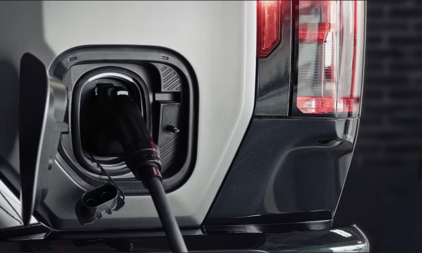 Closeup side image of a white 2026 GMC Hummer EV Pickup charging inside a home
