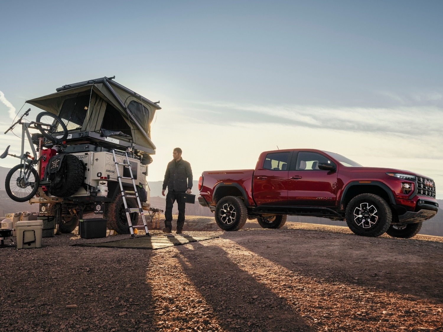 a man standing beside a red 2025 GMC Canyon truck with camping equipment