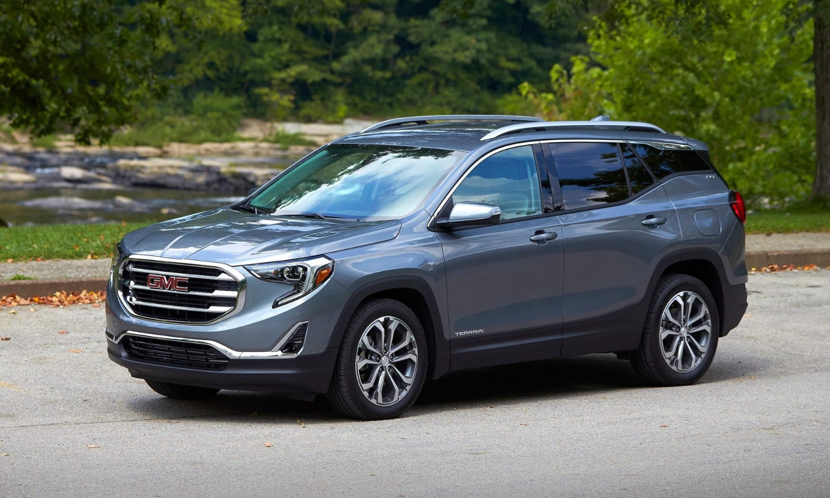 Exterior side image of a light blue 2018 GMC Terrain parked on a tree-lined suburban street