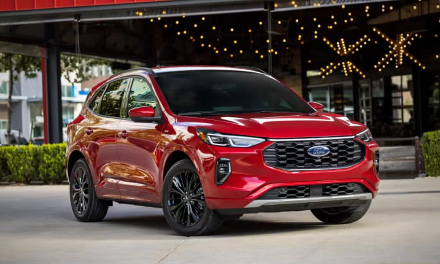 Exterior image of a red 2023 Ford Escape ST-Line Elite parked outside an illuminated shop on a sidewalk
