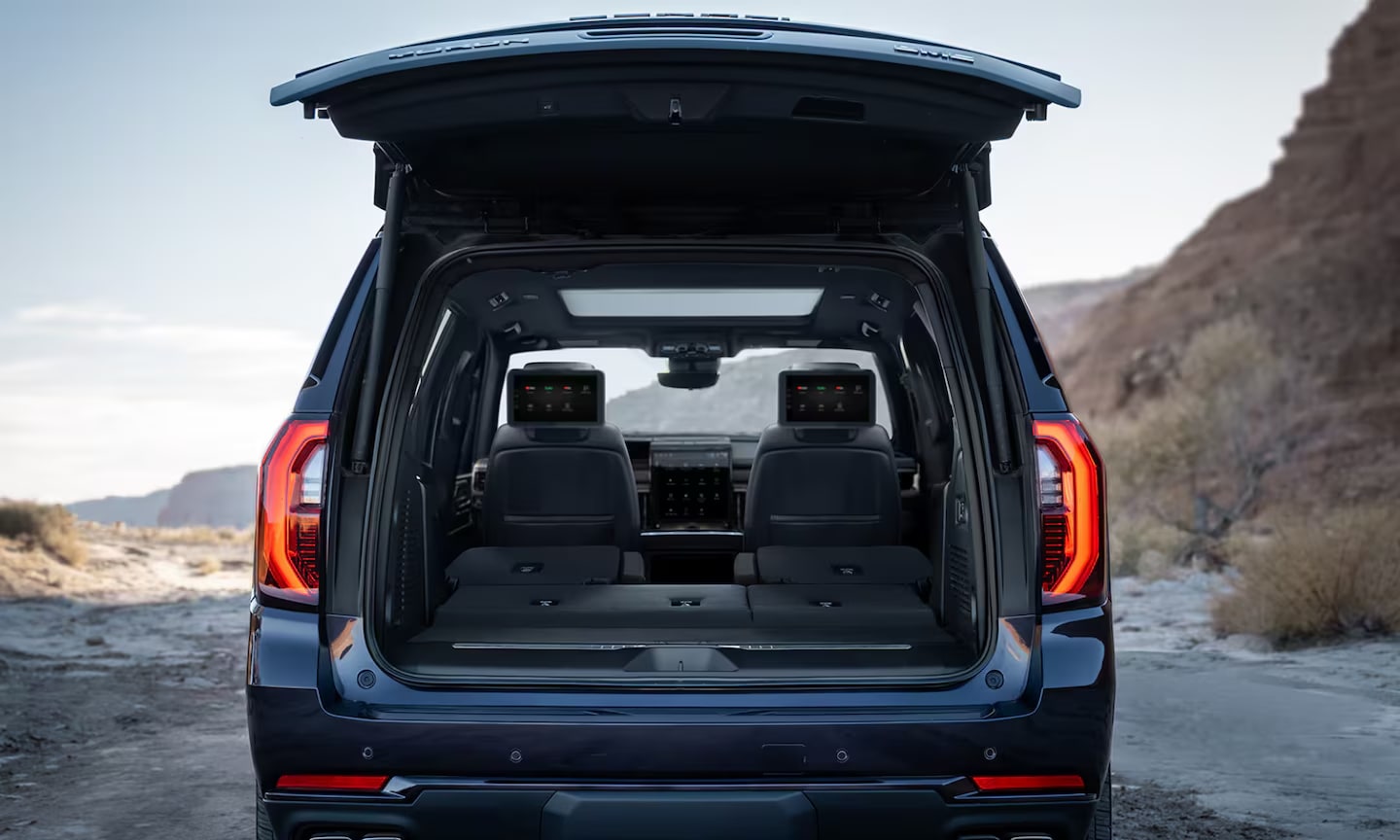 Exterior rear-view image of a blue 2026 GMC Yukon open trunk in a coastal setting