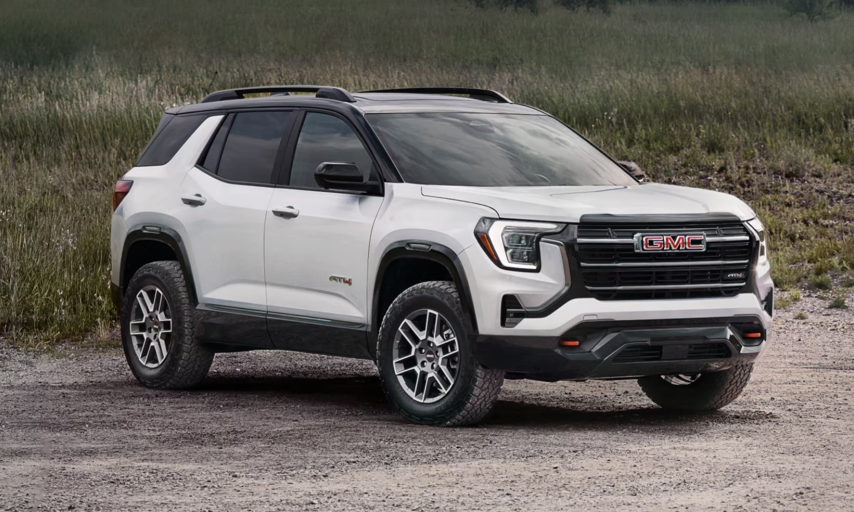 Exterior image of a white 2026 GMC Terrain AT4 outside on a gravel road with grass in the background