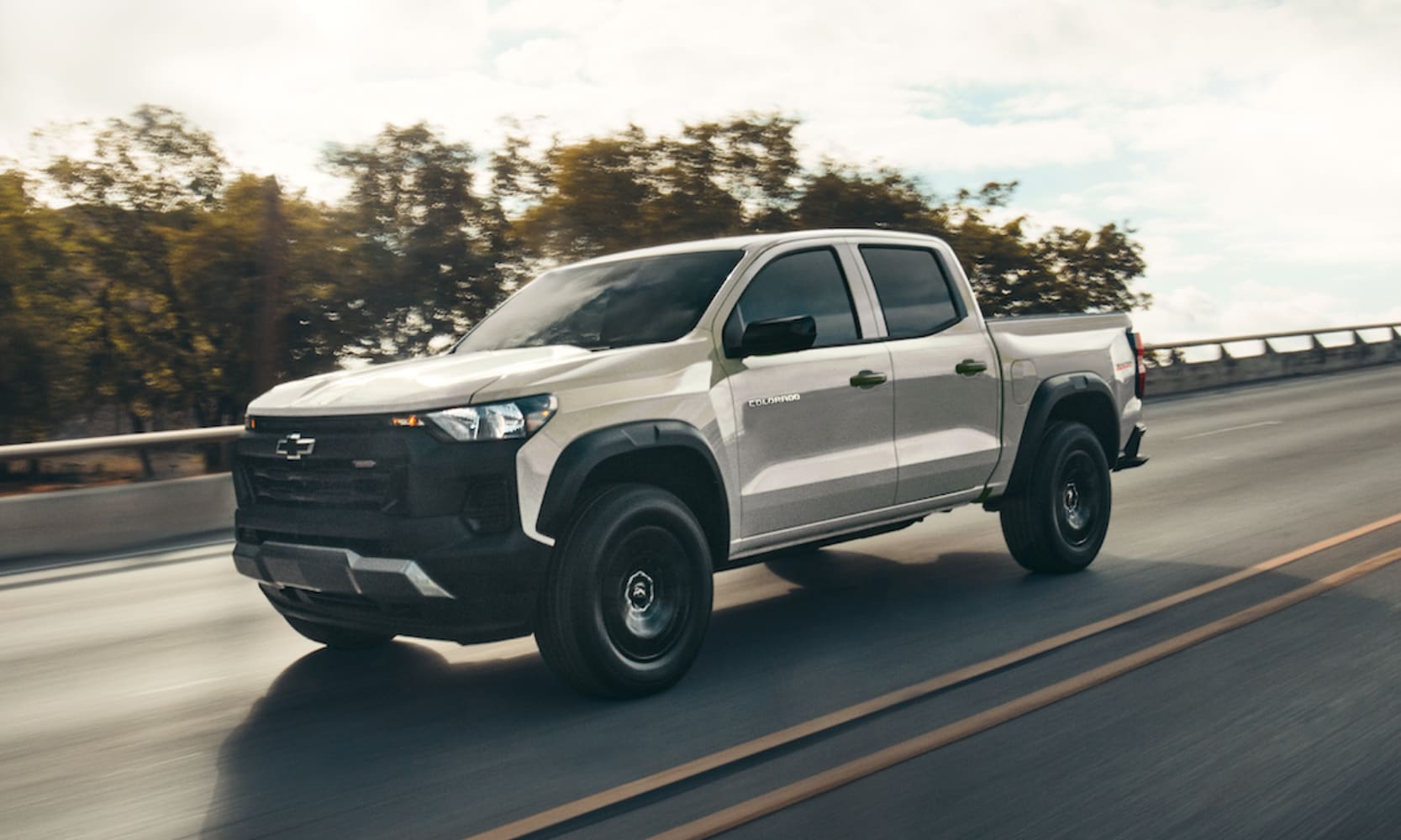 Exterior image of a white 2026 Chevy Colorado driving on an open tree-lined freeway