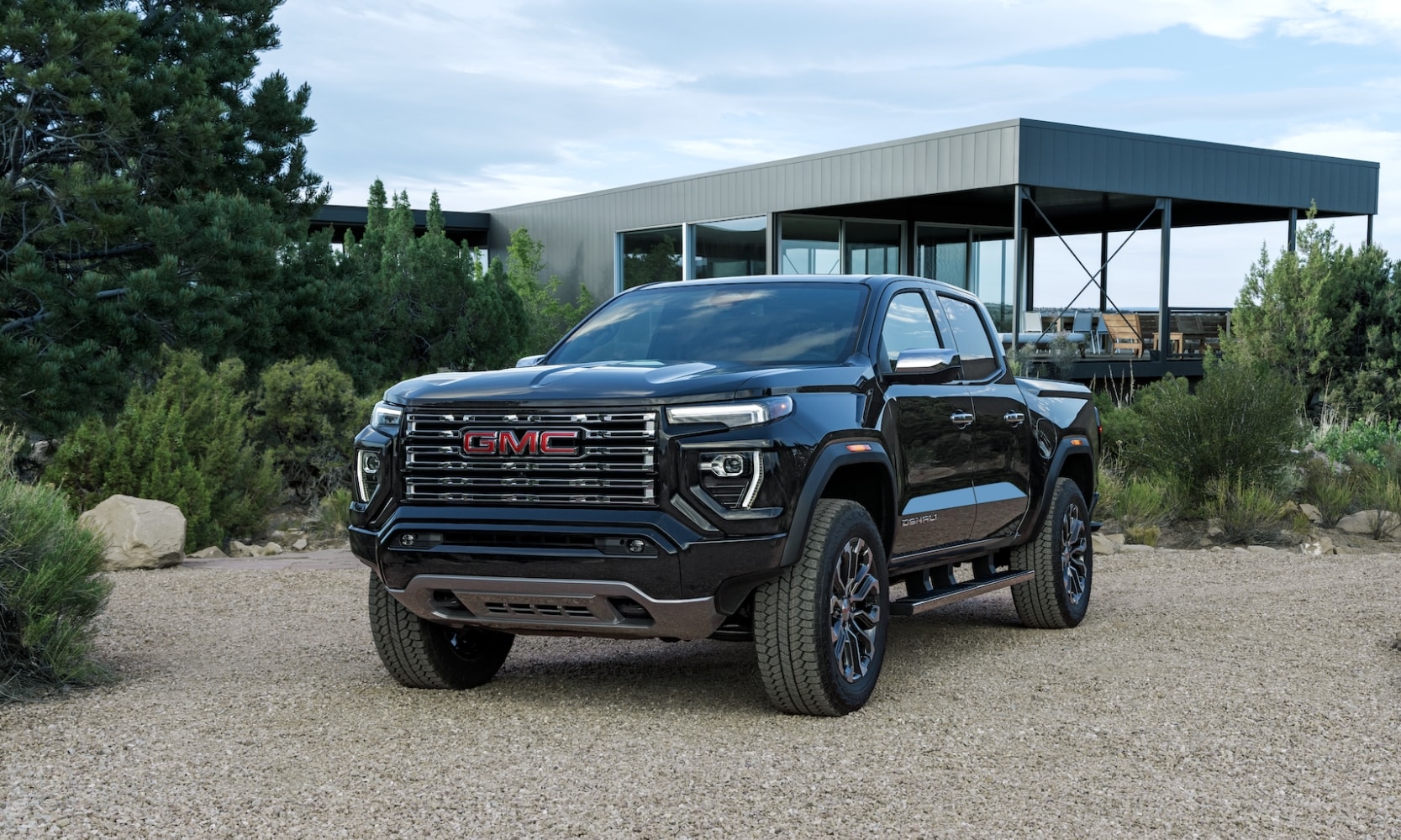 Exterior front side angle image of a black 2023 GMC Canyon Denali parked in a rocky residential driveway