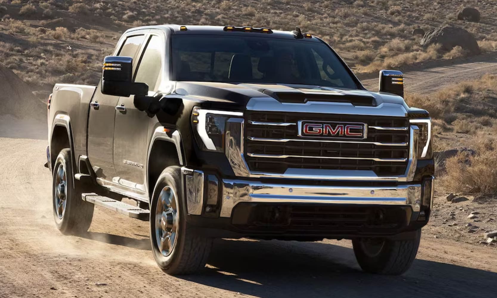 Closeup exterior image of a black 2026 GMC SierraHD SLT driving on an open dirt road