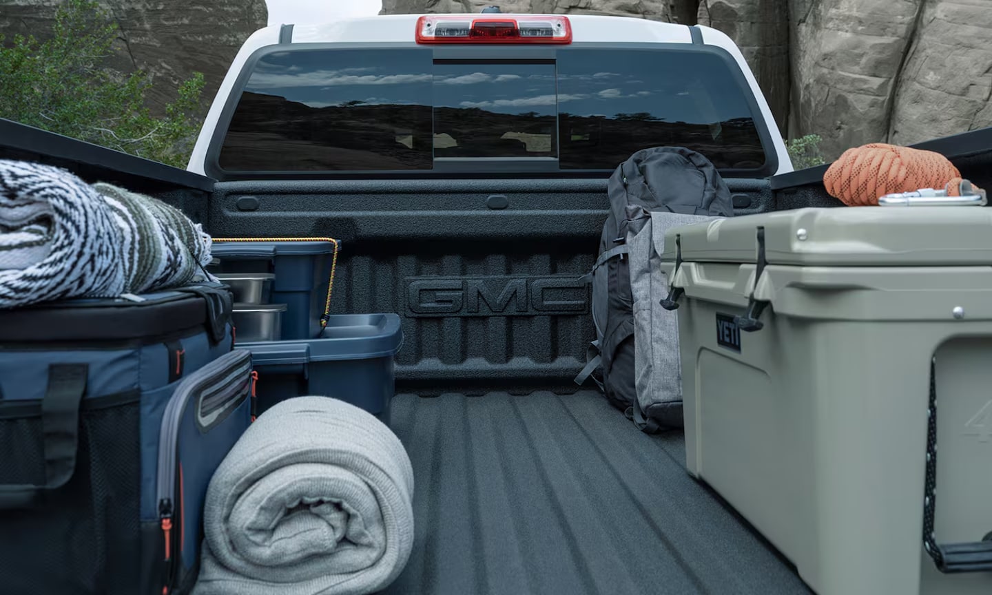 Close-up exterior image of a white 2026 GMC Canyon opened cargo bed with equipment on it