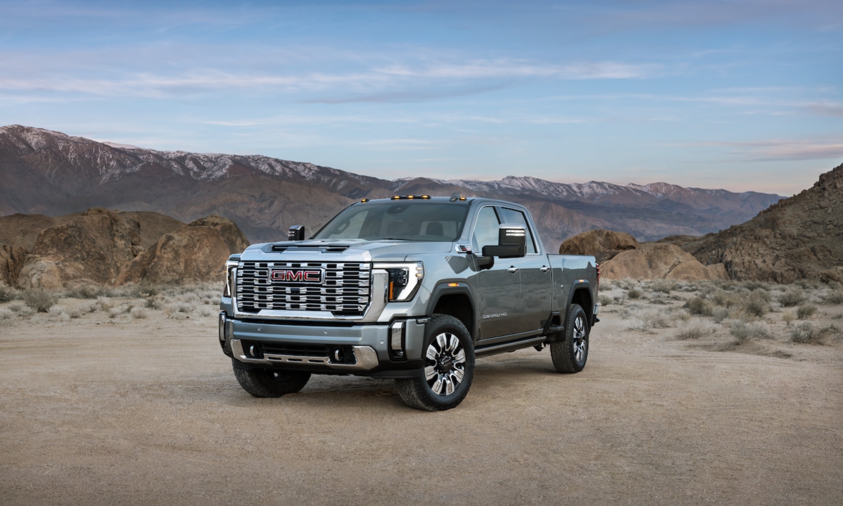 Exterior far view front image of a light blue 2026 GMC Sierra 2500 HD Denali Ultimate parked in a rocky mountainous landscape