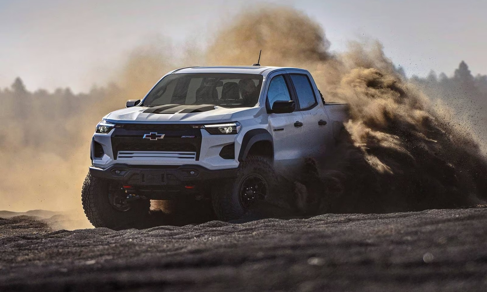 Exterior image of a white 2024 Chevy Colorado ZR2 Bison off-roading in a desert landscape with sand blowing