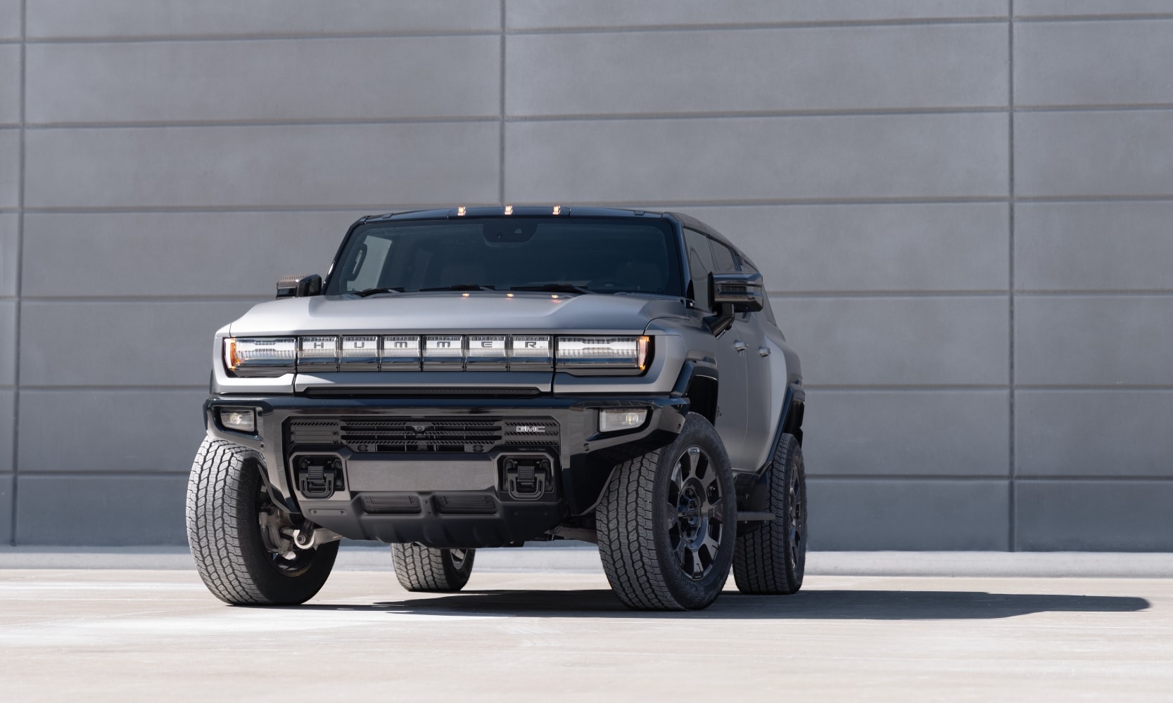 Exterior front image of a 2026 GMC Hummer EV SUV Carbon Fiber Edition parked in front of a concrete wall