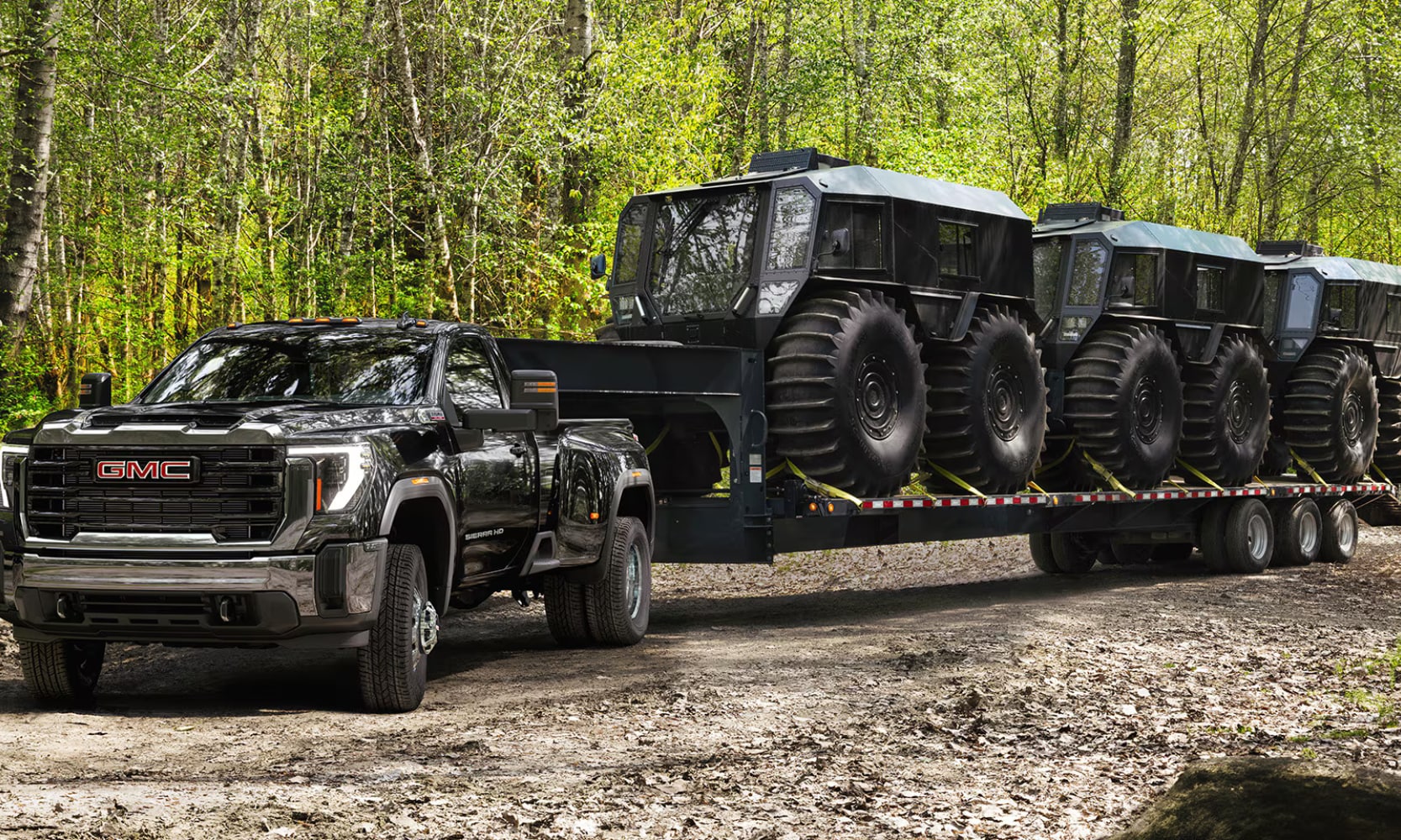 Exterior front angle image of a black 2026 GMC Sierra 3500 HD Pro towing three construction vehicles in a forest