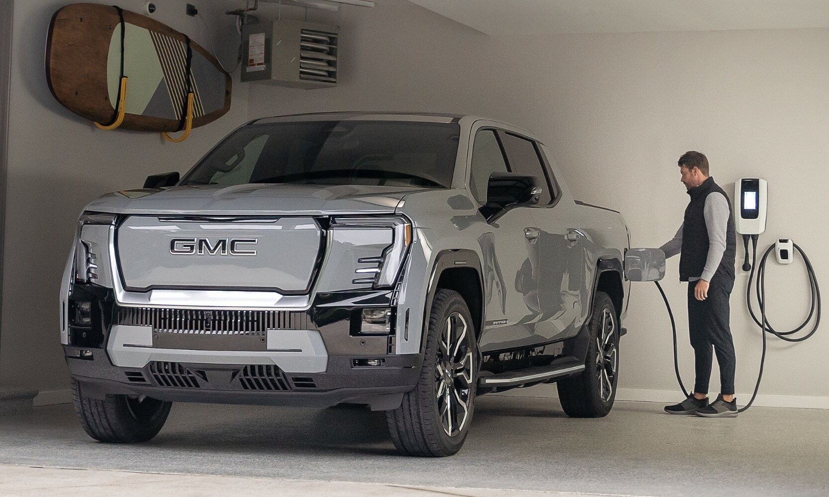 The 2025 GMC Sierra EV truck plugged up to a charging station recharging its battery inside of a home garage