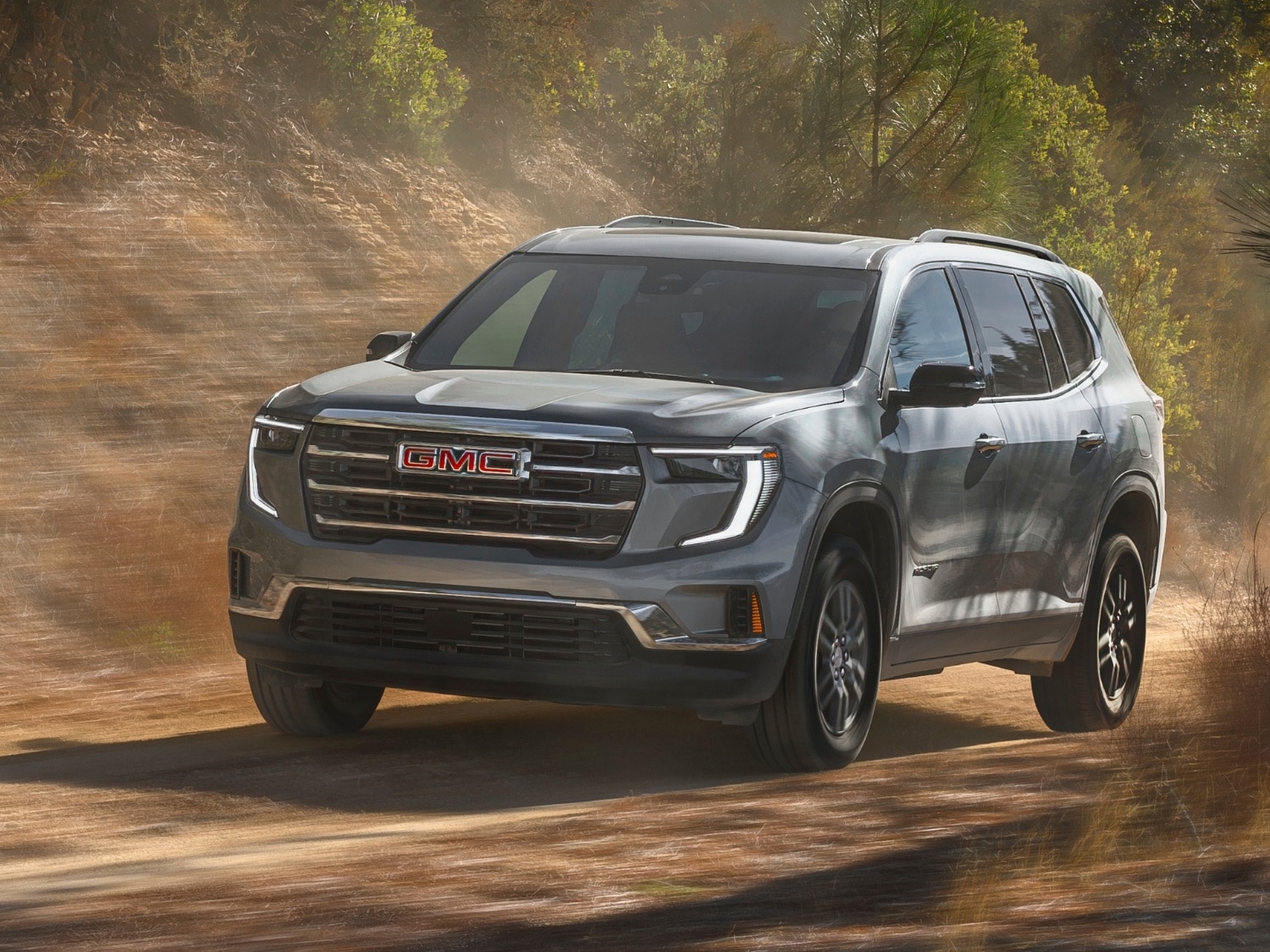 a 2025 GMC Acadia driving down a dirt path in the forest