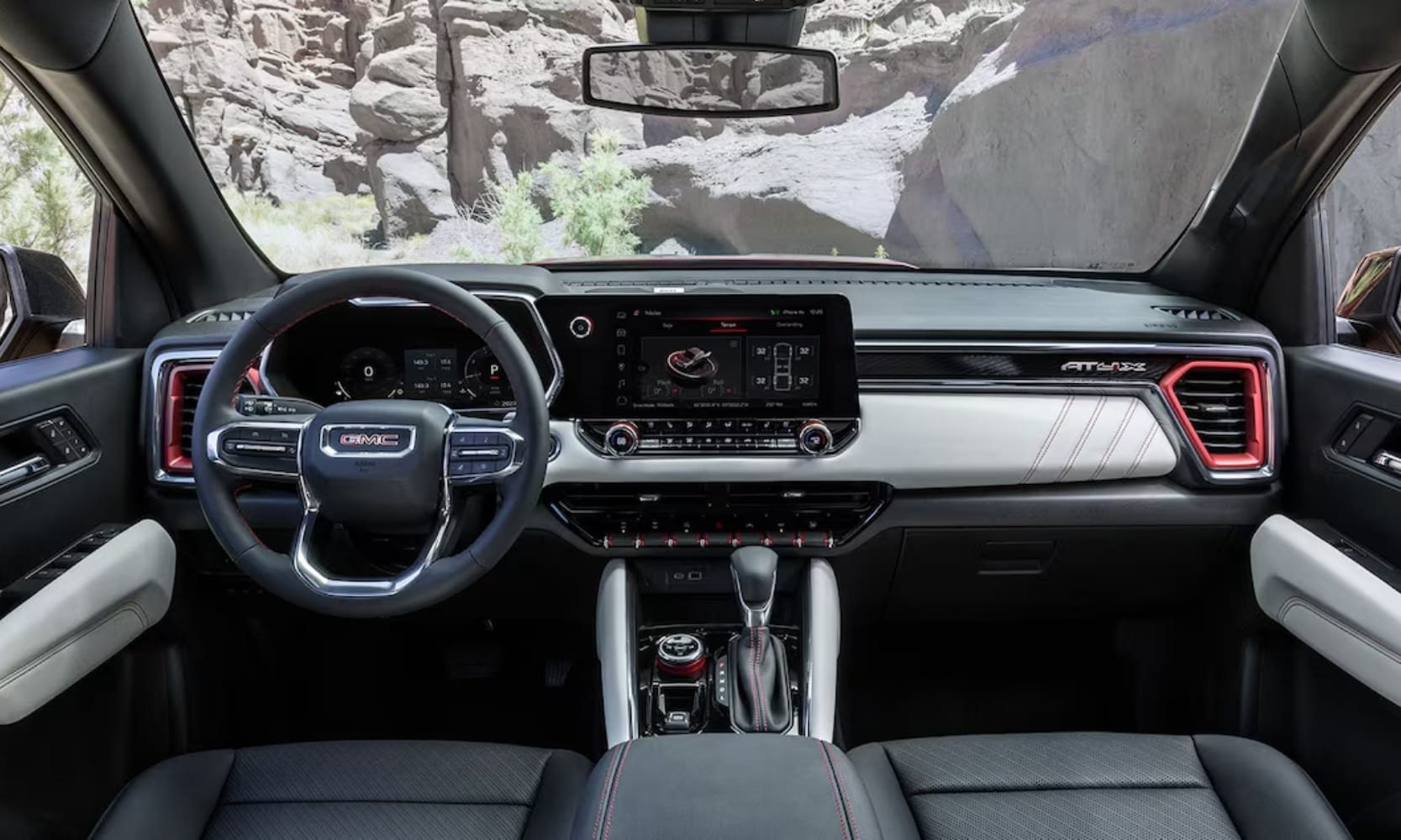 Interior image of a 2024 GMC Canyon AT4X front seats and dashboard area with rocky mountain views