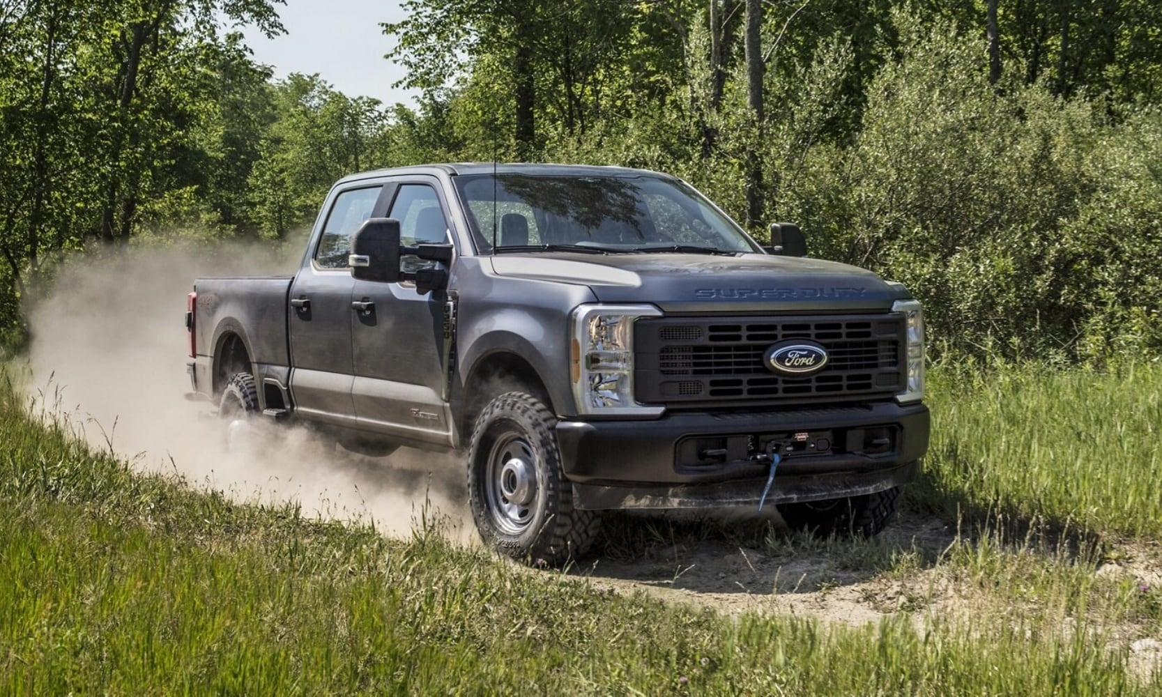 Exterior image of a dark gray 2025 Ford F-250 Super Duty off-roading on a dirt road in a rural landscape