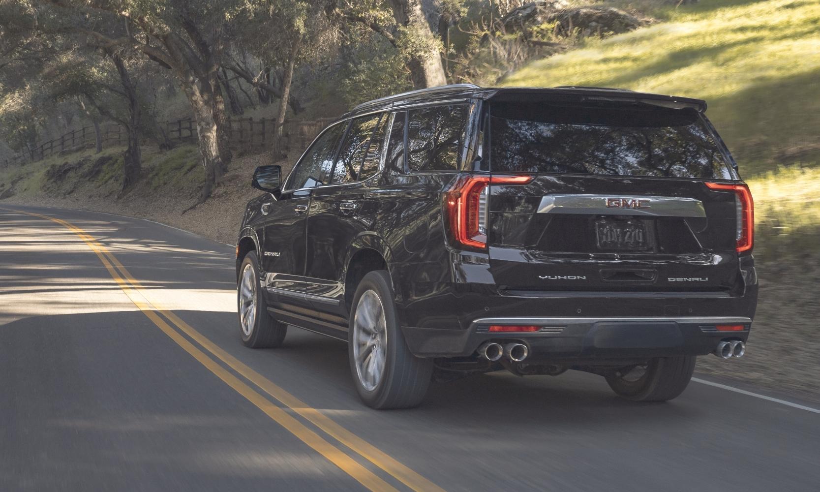 Rear exterior view of the 2023 GMC Yukon Denali driving down a road