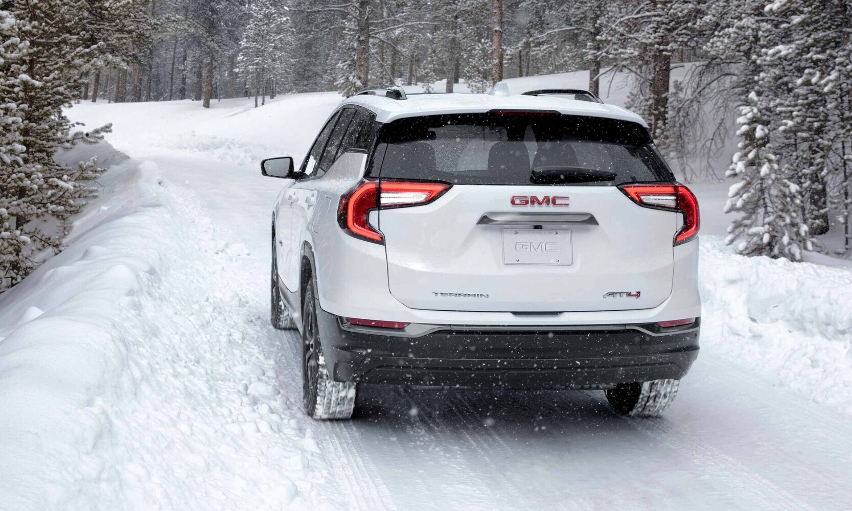 Rear exterior view of a 2023 GMC Terrain AT4 driving down an off-road path in heavy snow fall