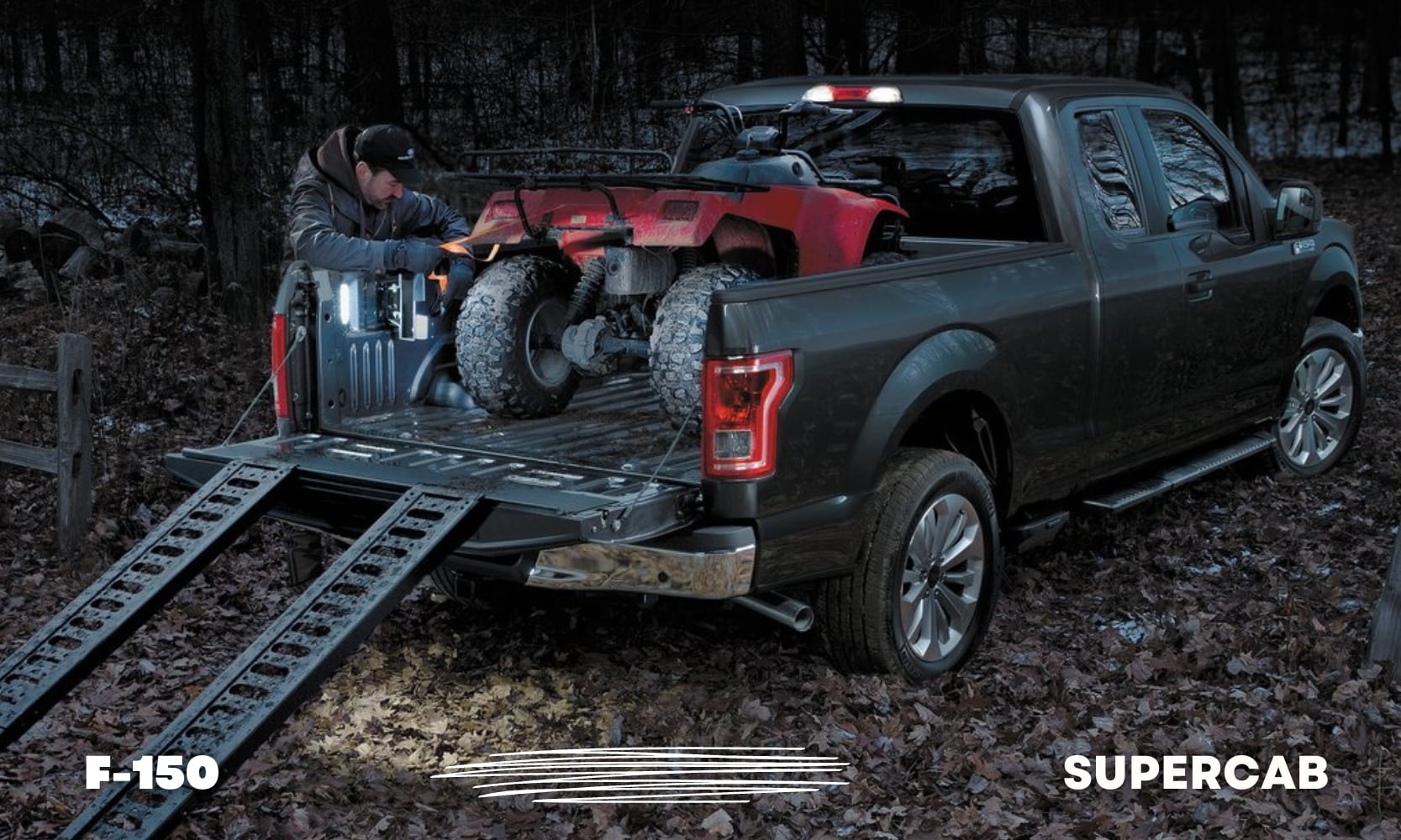 a dark gray used Ford F-150 SuperCab truck hauling an ATV in the truck bed parked in a forest with leaves on the ground