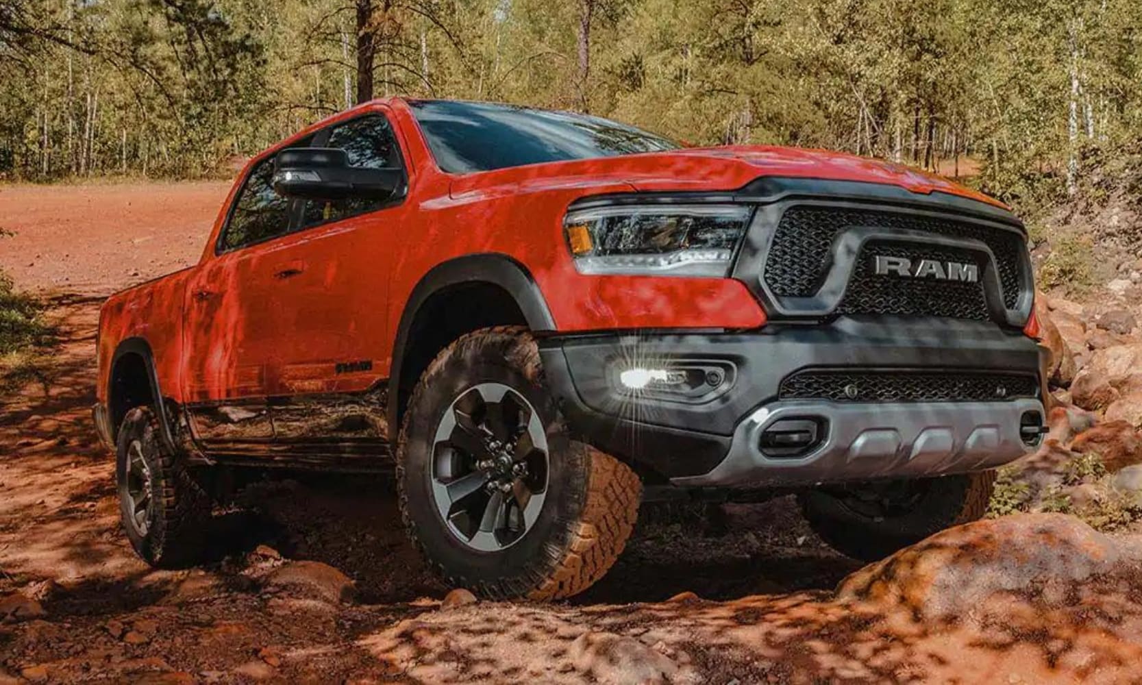 Exterior view of a 2022 Dodge Ram 1500 truck off-road in a forest driving over rocks