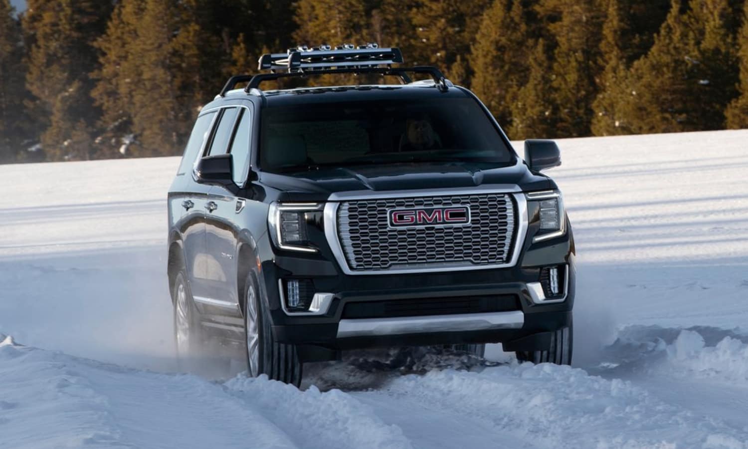 2022 GMC Yukon Denali luxury trim with mounted roof rack driving toward the camera lens through heavy snow