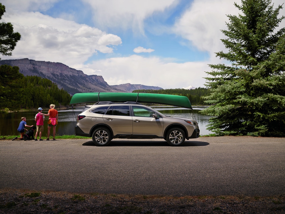 light gold Subaru Outback SUV parked next to a lake with a green kayak on the roof rack