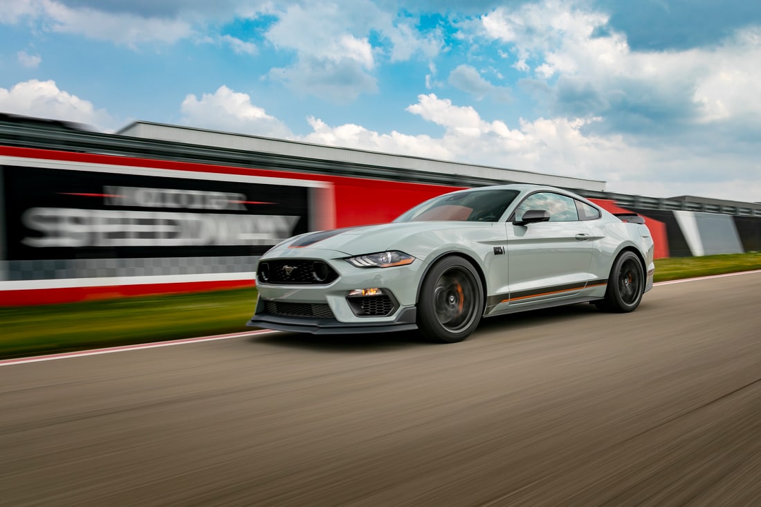 white Ford Mustang driving fast on a race track with a sponsor sign blurred in the background