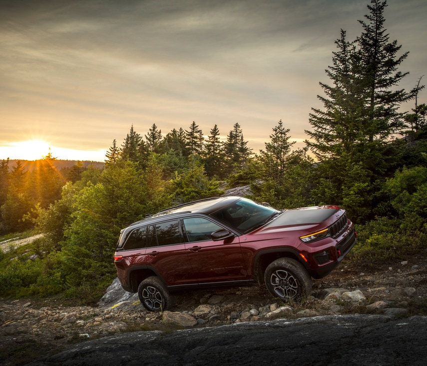 dark red Jeep Grand Cherokee SUV bouldering up a forest river