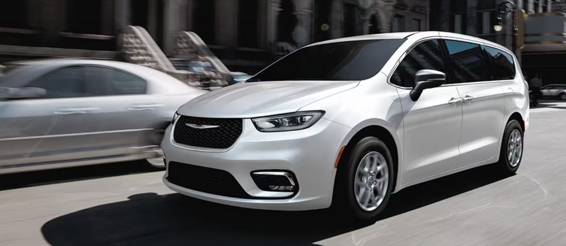 2026 White Chrysler Pacifica minivan driving on urban city street with motion blur