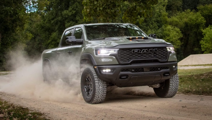 A green RAM 1500 driving down a dirt road and kicking up dust.