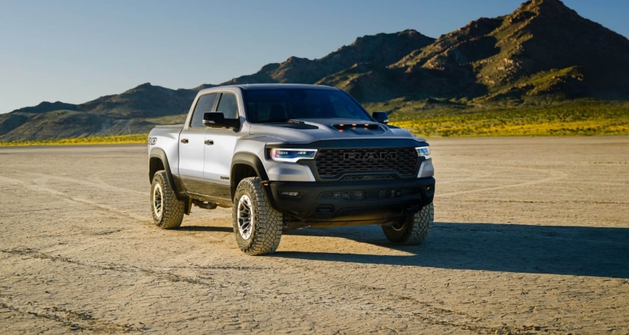 A silver RAM 1500 in a dirt clearing with mountain backdrop.