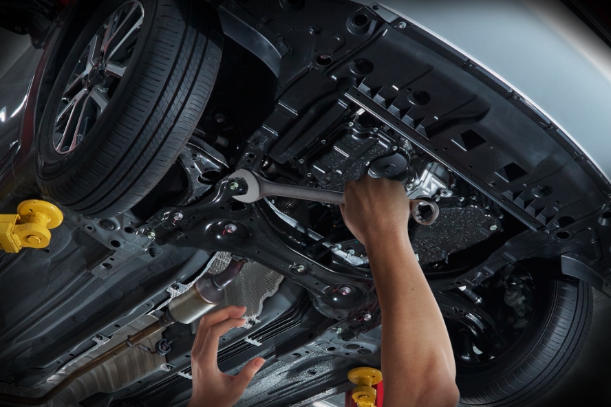 A technician working on the undercarriage of a car.