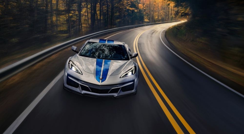 A silver 2024 Chevy Corvette E-Ray 3LZ driving on a winding tree-lined road