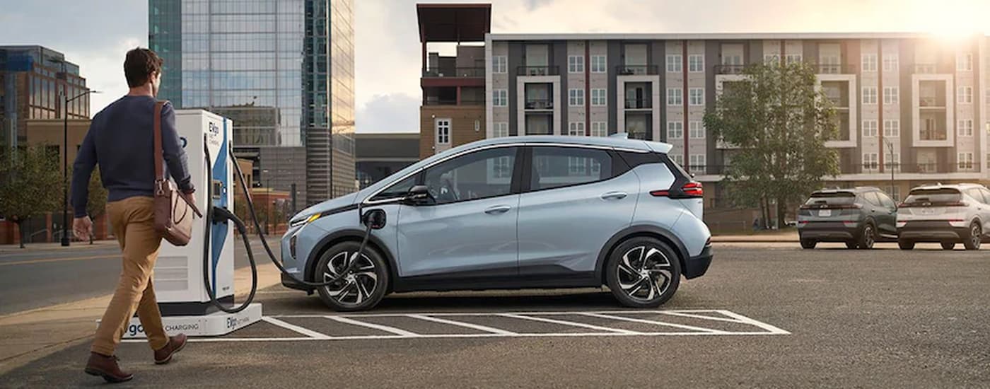 A man walks to a light blue 2022 Chevy Bolt EV parked at an electric charging station.