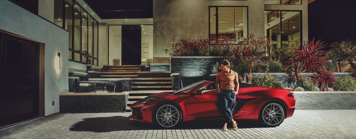 A man leaning against a red 2023 Chevy Corvette Z06 parked at a luxury home.