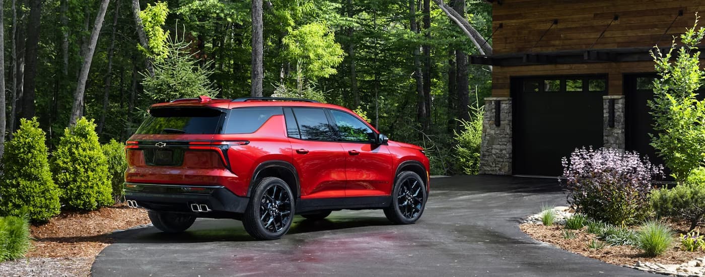 A red 2024 Chevy Traverse RS is shown from the rear parked in a driveway next to trees.