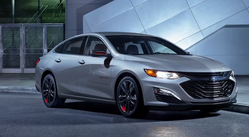 A silver 2024 Chevy Malibu 1LT is shown parked near a curb.