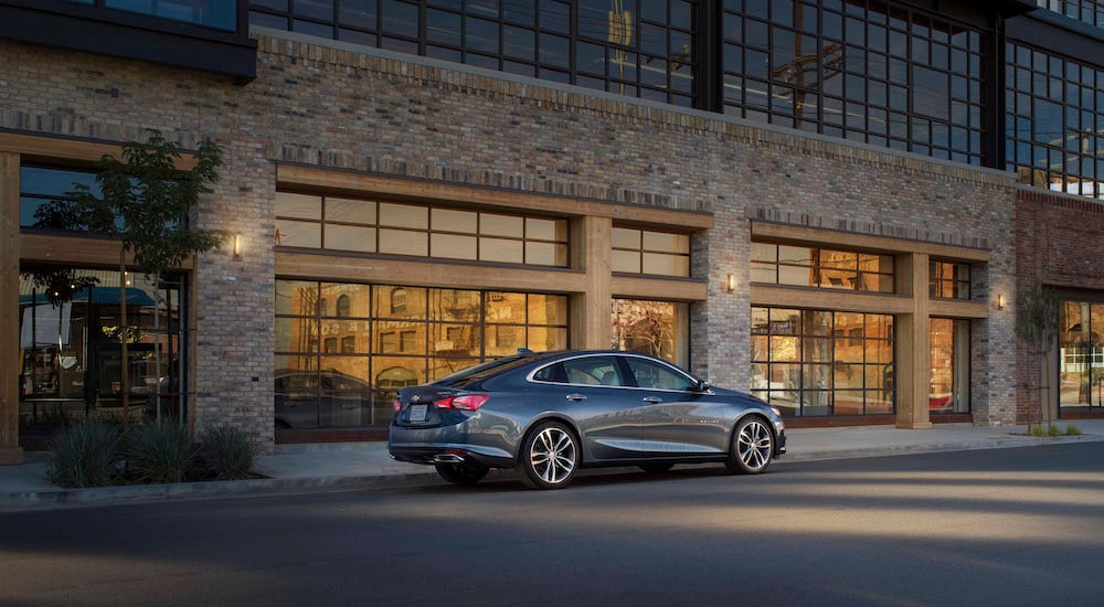 A grey 2023 Chevy Malibu for sale is shown from the side while parked.