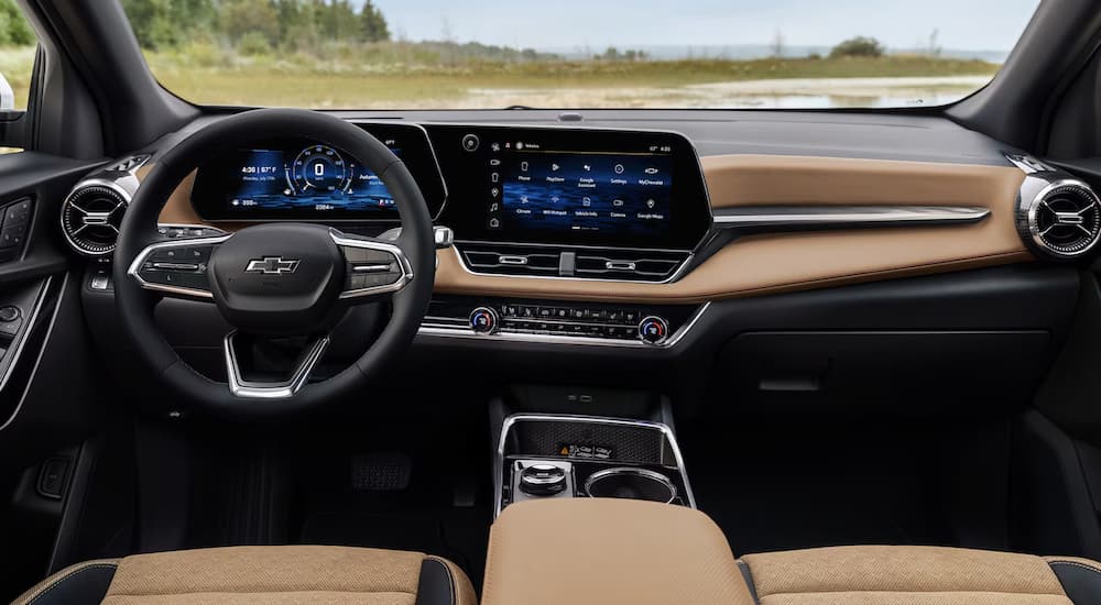 The black and tan interior of a 2025 Chevy Equinox with a view of the steering wheel and center console.