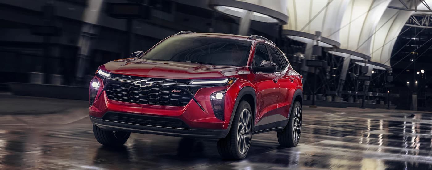 A red 2024 Chevy Trax RS driving on a city street at night after viewing Chevy SUVs for sale.