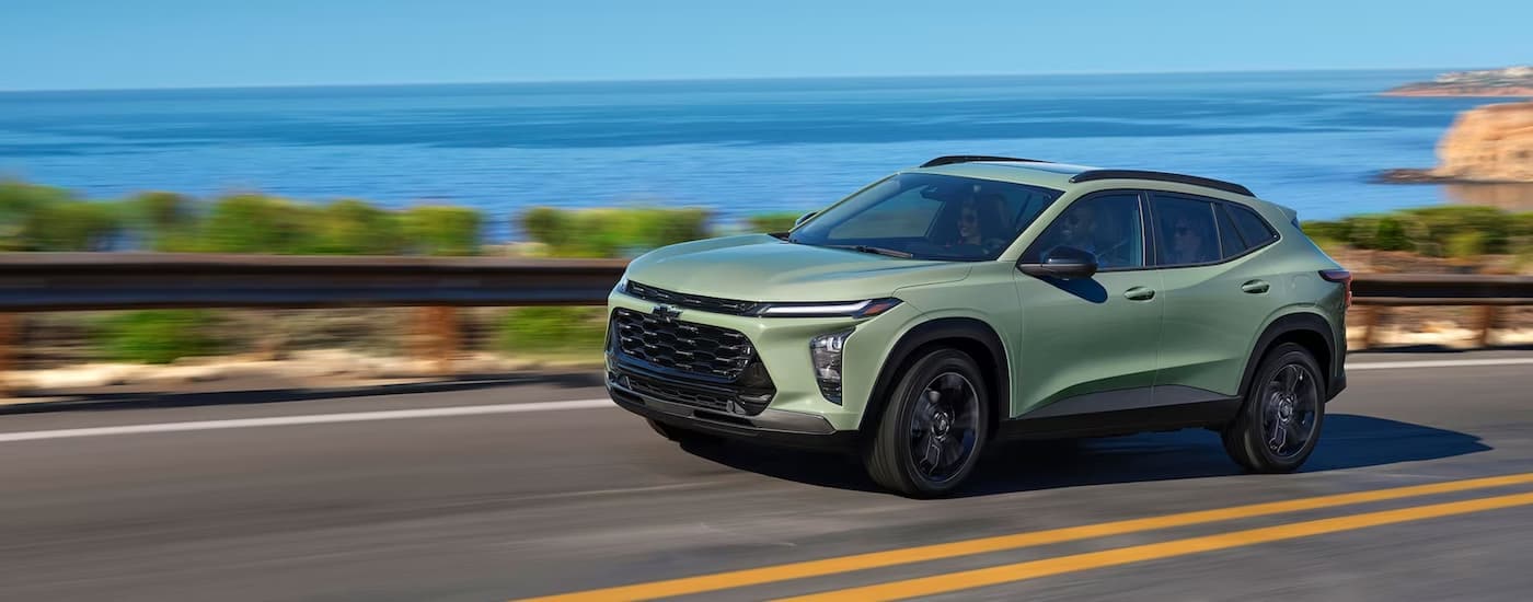 A green 2024 Chevy Trax is shown driving on a road next to an ocean after leaving a Bowie Chevy dealer.