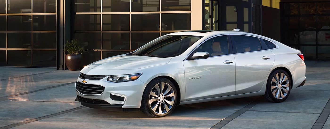 A white 2019 Chevy Malibu parked in front of a modern garage.