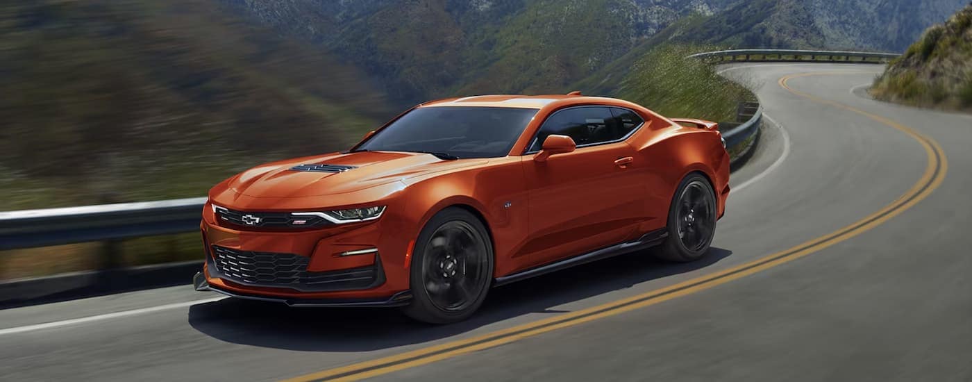 An orange 2024 Chevy Camaro 2SS is shown driving on a winding road after leaving a Waldorf Chevy dealer.