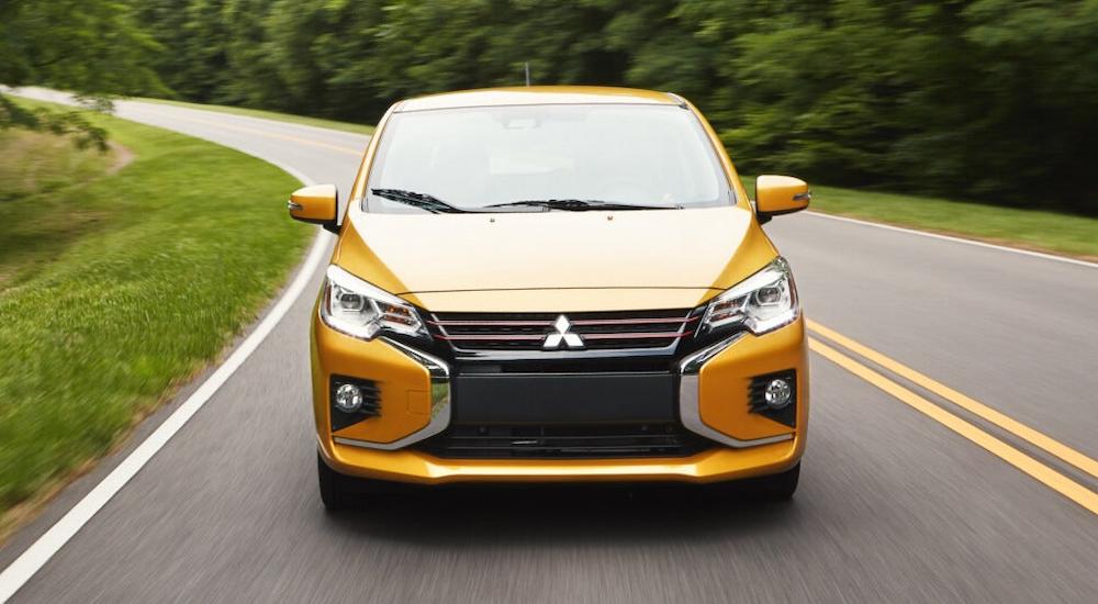 A yellow 2023 Mitsubishi Mirage driving towards the camera on a winding road.